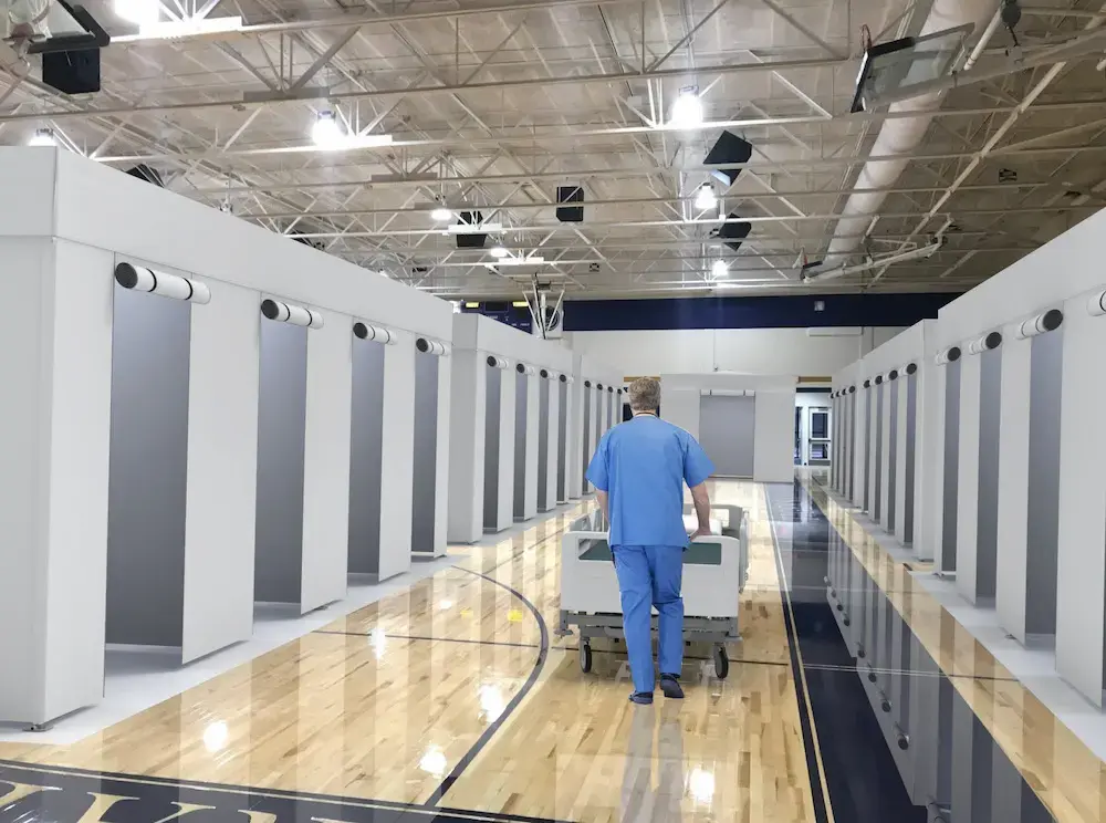 a medical carer pushing a hospital bed through a gymnasium with custom portable hospital tents with rolled up entrances